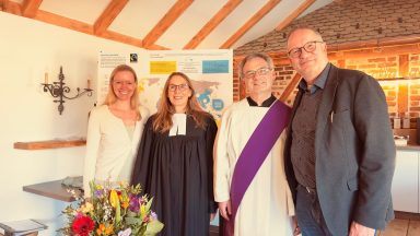 Vier Personen stehen zusammen, umgeben von Blumen und einem Informationsplakat.