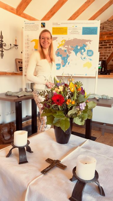 Frau mit Blumenstrauß steht vor einer Weltkarte und einem Tisch mit Kerzen.