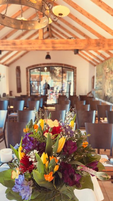 Bunte Blumen in einem eleganten Raum mit Tischen und Stühlen für eine Veranstaltung.